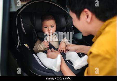 happy father is fastening safety belt to infant baby in the car seat Stock Photo