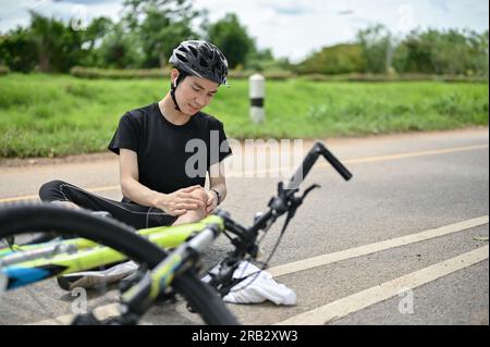 Asian male cyclist with injured knee carry bicycle walking in park ...