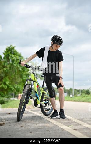 An injured young Asian male cyclist in sportswear and a bike helmet ...