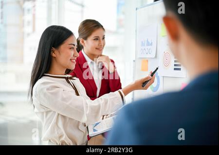 An attractive and confident millennial Asian businesswoman presented her marketing project on a whiteboard to her team in the meeting. creative brains Stock Photo