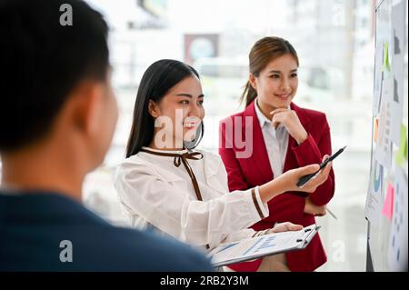 An attractive Asian businesswoman presented her marketing project on a whiteboard to her team in the meeting. creative brainstorming meeting concept Stock Photo