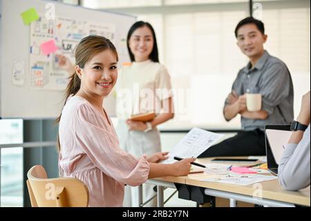 A beautiful millennial Asian female developer is in a meeting with her colleagues to plan a new mobile app project. Tech startup company concept Stock Photo