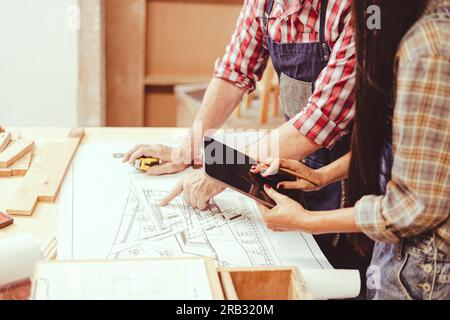 professional architect working with floor plan wooden home furniture and renovate in workshop talking consulting with engineer team. Stock Photo