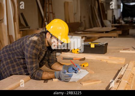 carpenter hispanic indian male wood worker furniture maker man looking paper plan designer in wood furniture factory. Stock Photo