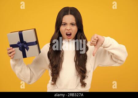 Angry face, upset emotions of teenager girl. Child teen girl with gift on yellow isolated background. Birthday, holiday present concept. Stock Photo