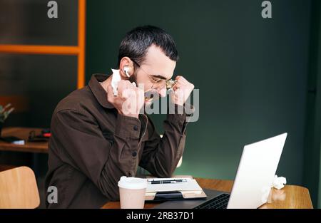 Angry bearded freelancer in cafe having failed again, talking on webcam, discussing problems with online business project, crumpling notebook pages Stock Photo