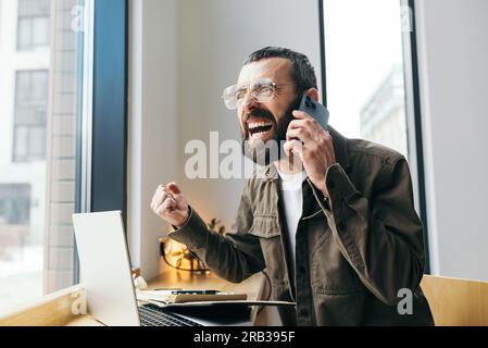 Angry caucasian male freelancer in cafe having quarrel during mobile phone conversation discussing problems with online business project Stock Photo