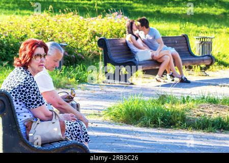 Minsk, Belarus - July 03, 2015: A contrasting scene in the park. Two couples on a bench - old and young Stock Photo