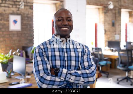 Portrait of happy african american casual businessman with arms crossed in office. Business, confidence and work, unaltered. Stock Photo