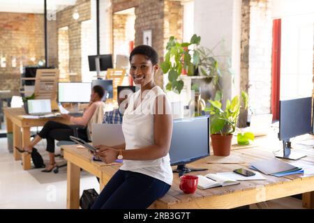 Portrait of happy african american colleagues with tablet in creative office. Business, technology, work and teamwork, unaltered. Stock Photo