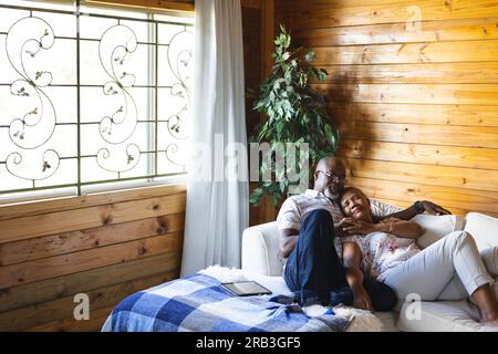 Senior african american couple lying on sofa and embracing at home. Senior lifestyle, relaxing and retirement, unaltered. Stock Photo