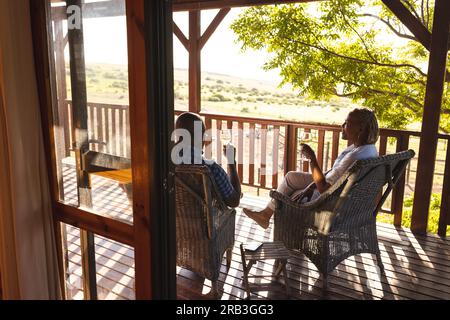 Senior african american couple drinking wine on sunny terrace. Senior lifestyle, relaxing, wellbeing in nature and retirement, unaltered. Stock Photo