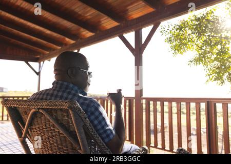 Senior african american man drinking wine on sunny terrace. Senior lifestyle, relaxing, wellbeing in nature and retirement, unaltered. Stock Photo