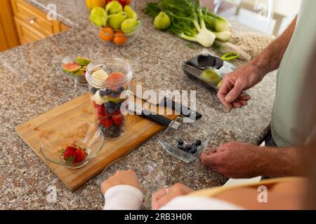 Hands of caucasian couple preparing and chopping fruits in kitchen. Healthy lifestyle, food and domestic life, unaltered. Stock Photo