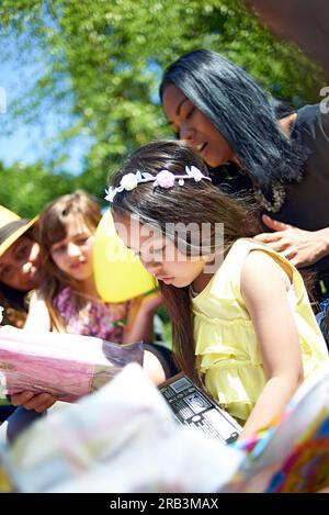 Cute little girl opening her birthday presents surrounded by friends Stock Photo