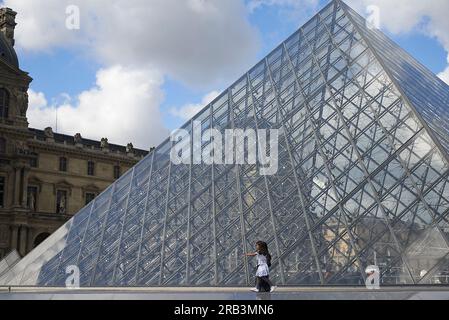 Asian girl and mother at glass pyramid building at the Louvre museum ...
