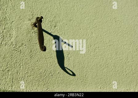 Holder for window shutter and its shadow against a green plastered wall. Stock Photo