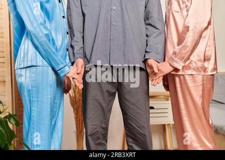 polygamy concept, cropped view of man holding hands with women at home, non traditional partners, freedom and diversity in relationship, acceptance an Stock Photo