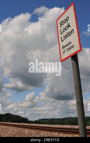 A Stop Look Listen warning sign at a public footpath crossing over a main railway line. Stock Photo