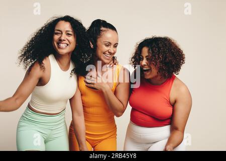 Group of diverse young female athletes are smiling and laughing as they stand together together in the studio dressed in sportswear, celebrating their Stock Photo
