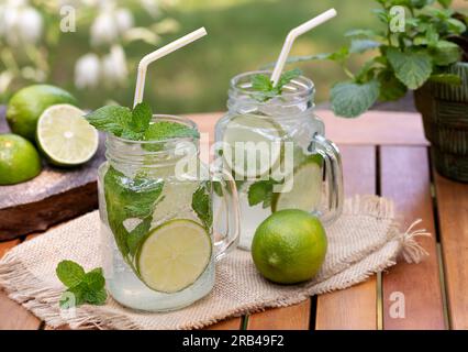 Mojito cocktail with lime slices and mint outdoors on wooden table with nature background Stock Photo
