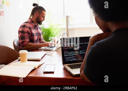 Over the shoulder shot of young woman developer typing code on laptop in office Stock Photo