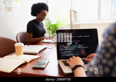Over the shoulder shot of young woman developer typing code on laptop in office Stock Photo