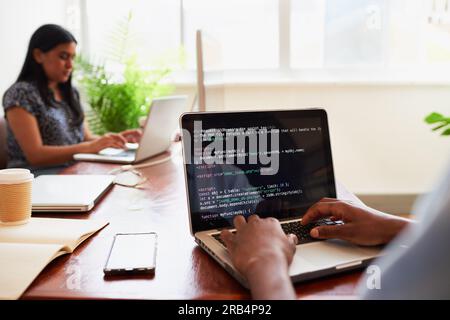 Over the shoulder shot of young male developer typing code on laptop in office Stock Photo