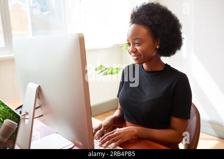 Beautiful Black woman working at desk in office, developer in tech start up Stock Photo