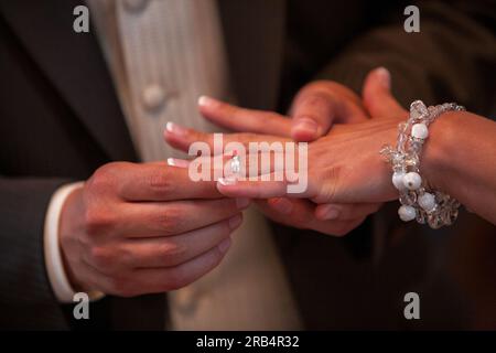 A heartfelt close-up photograph capturing the tender moment of a loving bride and groom exchanging beautiful wedding rings. The image evokes emotions of commitment and devotion, embodying the 'Marry Me' concept in a touching and timeless manner. Close up of loving bride and groom putting a beautiful wedding ring to the beloved partner, marry me concept. High quality photo Stock Photo