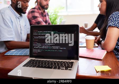 Close up of laptop screen with code, developers meeting boardroom table talking Stock Photo