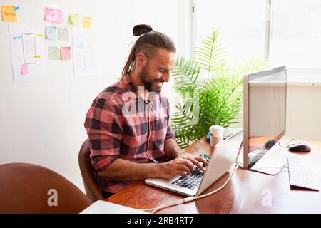 Senior developer works in open plan creative office, man bun hipster look Stock Photo