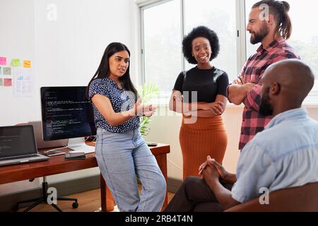 Diverse group of colleagues standing and chatting in the office, coding company Stock Photo