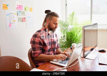 Senior developer works in open plan creative office, man bun hipster look Stock Photo