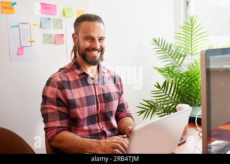 Senior developer works in open plan creative office, man bun hipster look Stock Photo