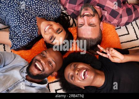 Close up overhead shot of group of friends posing for camera, lying on rug Stock Photo