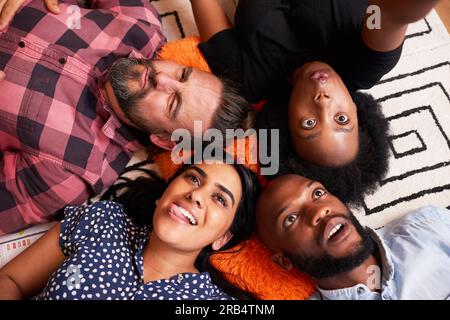 Diverse group of friends lying down taking silly selfies in circle, pulling face Stock Photo