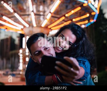 Young happy couple taking selfie while having fun at night in an amusement park Stock Photo