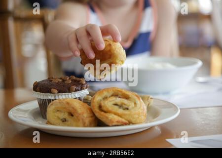 Close up of child's hand taking pastry from plate Stock Photo