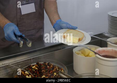 Buffet style service - Canteen worker at serving line putting food on the plate Stock Photo