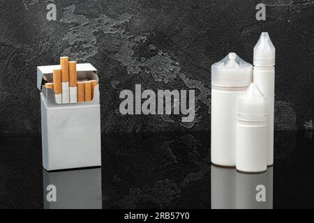 Pack of cigarettes and e-juice liquid bottles on black background Stock Photo