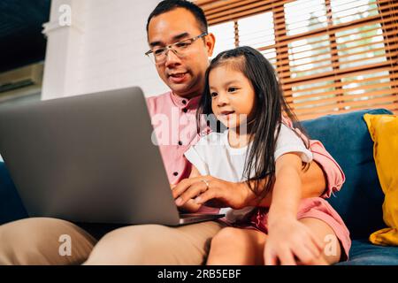 Father using laptop playing with daughter in living room Stock Photo