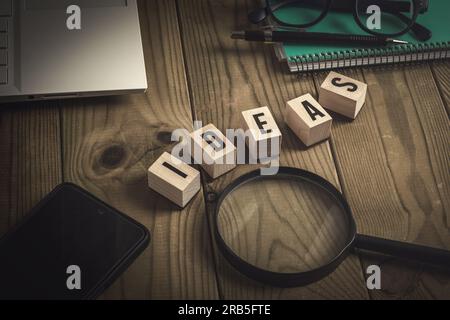 Wooden cubes forming the word ideas on a wooden table with a laptop, a mobile phone, a magnifying glass, a notebook and glasses, tools to develop and Stock Photo