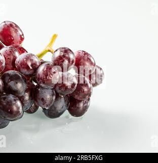 Wet bunch of dark grapes with water drops on the berries on a white background Stock Photo