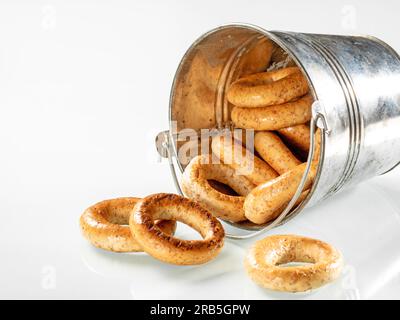 A pile of crispy pretzels pouring out of a metal bucket lying on its side on a white background. Stock Photo