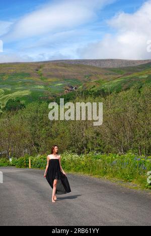 A woman in a flowing, black dress walks down a path by Mt, Esja, Iceland. Stock Photo