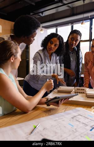 Diverse female architects in discussion using model, blueprints and tablet in casual office meeting. Casual office, teamwork, business, lifestyle, des Stock Photo