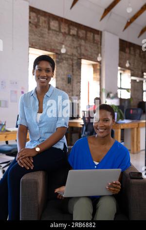 Portrait of happy african american colleagues using laptop in creative office. Business, technology and teamwork, unaltered. Stock Photo