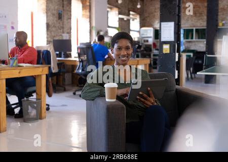 Portrait of happy african american colleagues using computer and tablet in creative office. Business, technology and teamwork, unaltered. Stock Photo