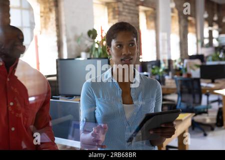 African american colleagues using tablet and discussing work in creative office. Business, technology and teamwork, unaltered. Stock Photo